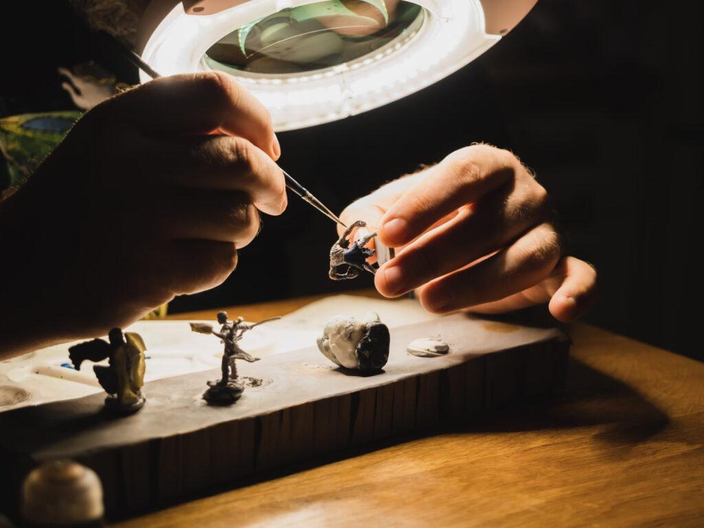 human hands painting under the lamp with light and magnifying glass plastic minifigures for board games