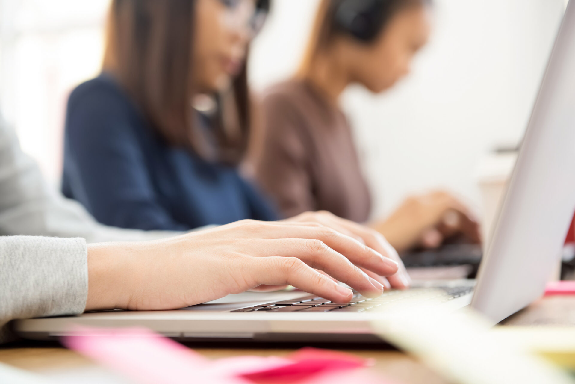 Hands of female students using laptop computer learning and searching information on the internet with her classmates aside